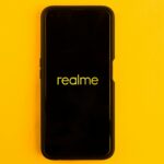 In this photo illustration the Realme logo seen displayed on a smartphone and on the background
